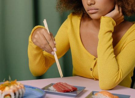 A woman in a yellow top eating sushi with chopsticks, featuring nigiri and sashimi.