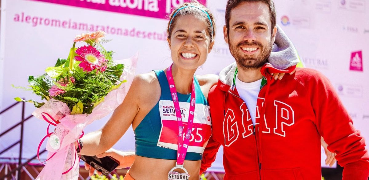 Smiling marathon winner with medal and flowers celebrates with friend.