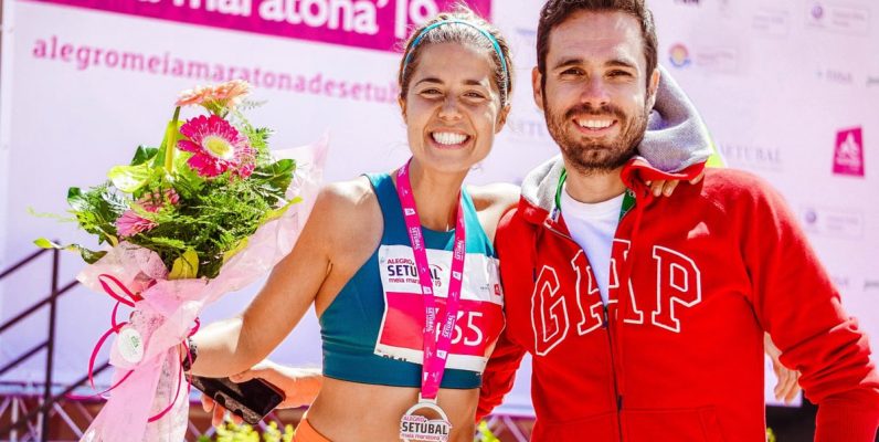 Smiling marathon winner with medal and flowers celebrates with friend.